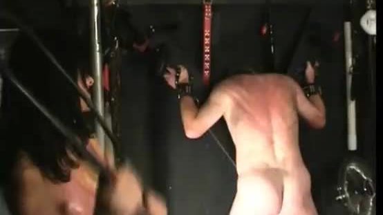 Dirty slave tied to a wall is hit with a whip on his back by hot mistress with big fake boobs